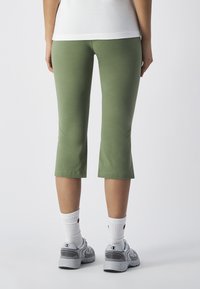 Zielone legginsy capri wykonane z elastycznej tkaniny, o dopasowanym kroju, skróconej długości i gładkiej fakturze. Noszone z szarymi sneakersami i białymi skarpetkami.