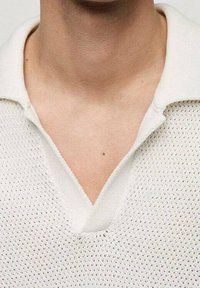 Polo blanc en maille avec un tissage texturé, doté d'un col en V et de manches courtes. Les détails incluent un motif subtil et un tissu doux.