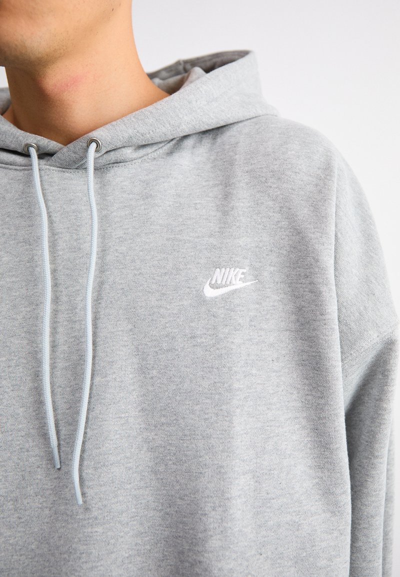 Szary polarowy sweatshirt o miękkiej teksturze, z białym haftowanym logo Nike na piersi oraz sznurkami w jaśniejszym odcieniu szarości.