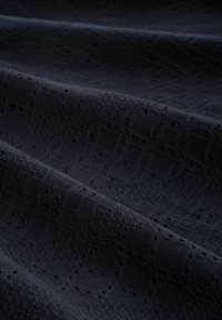 Tmavě námořnická tkanina s texturovaným vzorem obsahujícím geometrické tvary a malé výřezy, vytvářející vrstvený vzhled.