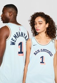 Šviesiai mėlyni krepšinio marškiniai su juodu tekstu „WEMBAANYAMA“ ir „SAN ANTONIO“. Papuošti rožiniais akcentais. Nike logotipas yra.