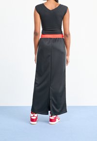 Svart åtsittande topp med korta ärmar, kombinerad med en lång svart kjol med ett rött elastiskt midjeband och en sidoklyfta, bärs med röda sneakers.