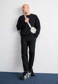 Sort stribet sweatshirt, sorte bukser og sorte sneakers med fed "RIP" på siden. Lille hvid crossover taske med lynlåsdetalje.