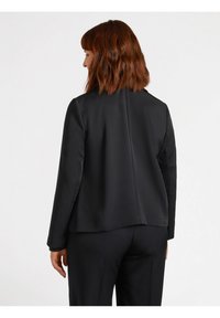 Blazer nero con una texture liscia, design sartoriale e linee pulite. Caratterizzato da maniche lunghe e un collo alto, mostrato dal retro.