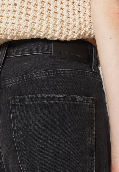 Black denim jeans feature a back pocket and a visible label "Citizen + Humanity." The fabric has a slightly distressed texture.