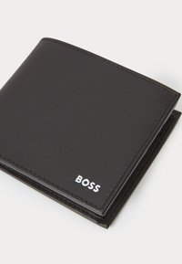 Zwarte leren portemonnee met wit "BOSS" logo. Heeft een gladde textuur en nette stiksels, opvouwbaar ontwerp voor kaart- en biljetopslag.