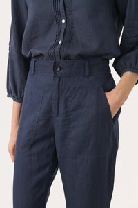Camicia in lino blu navy con fronte bottonato, caratterizzata da pieghe testurizzate e maniche a palloncino; abbinata a pantaloni blu navy con tasche.