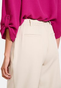 Roze textuurblouse met opgerolde mouwen, gecombineerd met crèmekleurige wijde broek met een zachte tailleband en twee achterzakken.