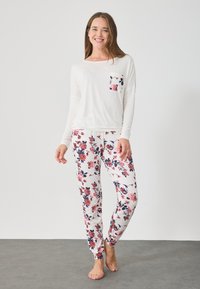 Μακρυμάνικο λευκό μπλουζάκι με λουλούδι στη τσέπη, σε συνδυασμό με στενά παντελόνια με floral σχέδιο σε λευκό, ροζ και ναυτικό μπλε. Μαλακό βαμβακερό ύφασμα.