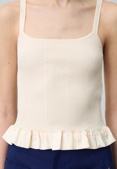 Débardeur ribbed beige avec des bretelles fines, doté d'un ourlet volé. Le tissu a une texture douce et un motif vertical subtil.