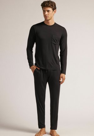 Haut noir à manches longues avec une poche poitrine, associé à un pantalon noir à taille élastique assorti, tous deux fabriqués dans un tissu lisse et confortable.