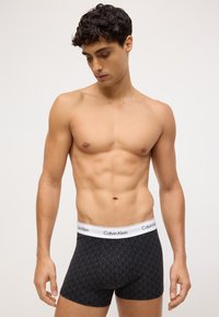 Czarne bokserki z geometrycznym wzorem, z białą gumką z logo Calvin Klein. Miękka tkanina, dopasowany krój.