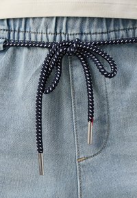 Marinblå och vit flätad dragsnörning knuten i en rosett på ljusblå denimbyxor med metalländar.