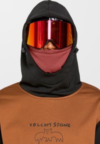 Vêtement à capuche noir avec des accents marron, présentant un design graphique et de grandes lunettes de ski rouges. Tissu lisse et texturé.