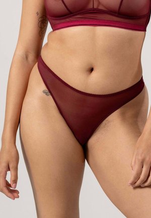 Burgundy genomskinlig tanga med en slät yta, med låg midja och elastisk midjeband, som framhäver huden genom tyget.