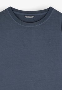 Tricou bleumarin din bumbac moale, cu guler rotund și un mic logo brodat pe piept. Textură netedă și design casual.