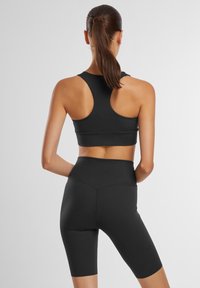 Sort sportsbh med racerback-design og højhalsede sorte shorts, begge lavet af strækbart materiale, der viser en sømløs finish.