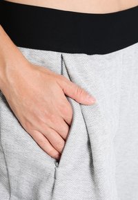 Lichtgrijze sweatpants met een gestructureerd visgraatpatroon, voorzien van een zwarte elastische tailleband en een ritssluiting aan de zijkant.