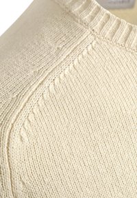 Crème-kleurige gebreide trui met een ribbelkraag en een textuurpatroon met subtiele details langs de naden.