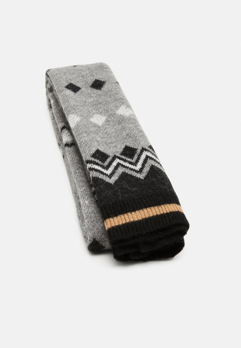 Chaussettes gris à motifs avec des dessins géométriques noirs et blancs, dotées d'un revers côtelé noir souligné d'une fine bande dorée.