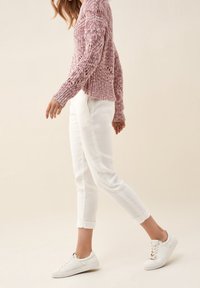 Hellrosa Strickpullover mit offenem Muster, kombiniert mit weißen, umgeschlagenen Hosen und weißen Sneakers. Der Pullover hat lange Ärmel und eine lockere Passform.