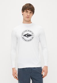 Λευκή μακρυμάνικη μπλούζα surf με στρογγυλό λογότυπο σε μαύρο σχέδιο, με την κείμενο "Rip Curl Surf Co Established 69" στο κέντρο.