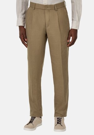 Pantaloni in lino beige con una vestibilità dritta, pieghe singole e chiusura con bottone. Abbinati a sneaker casual di colore chiaro.