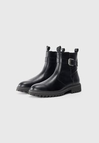 Las botas de cuero negro a la altura del tobillo cuentan con un acabado suave, un detalle de hebilla rectangular y suelas de goma texturizadas con un patrón de relieve.