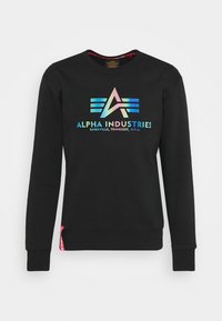 Felpa nera con maniche lunghe, polsini a coste e collo rotondo. Presenta un logo con gradiente di colore e il testo "ALPHA INDUSTRIES", e un'etichetta rosa all'orlo.