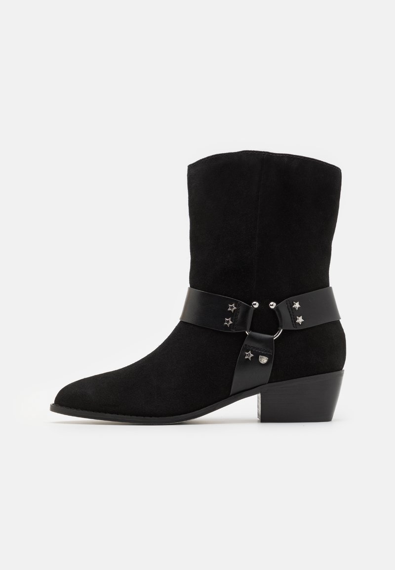 Black suede ankle boot with a curved toe, featuring a black leather strap accented with silver stars, and a chunky heel.
