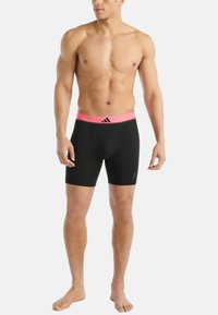 Svarta träningsshorts med ett brett rosa midjeband som har en logotyp. Tyget ser jämnt och åtsittande ut, designat för rörelse och komfort.