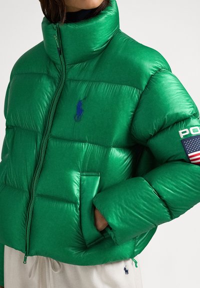 Zelena puhasta jakna z visokim ovratnikom, prešitim vzorcem, zadrgo in modnim logotipom. Levi rokav ima značko z ameriško zastavo in besedilom.