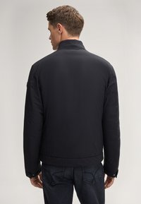 Giacca nera imbottita con colletto alto e polsini elasticizzati, caratterizzata da una texture liscia e da un design semplice e lineare.