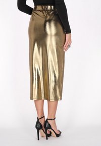 Rok mid-length emas metalik dengan pinggang yang pas, tekstur halus, dan sedikit kilau. Dipadukan dengan sandal hak tinggi hitam.