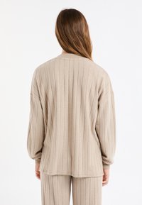 Beżowy prążkowany sweter rozpinany o luźnym kroju, z długimi rękawami i okrągłym dekoltem. Miękka faktura i subtelne, pionowe zdobienia.