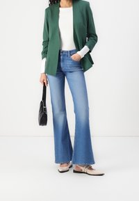 Zelený blejzr s řasenými rukávy, bílý top, světle modré rozšířené džíny, béžové vysoké boty a malá černá kabelka.