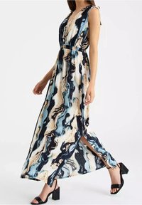 Maxi sukienka w marmurkowy wzór w odcieniach niebieskiego, kremowego i czarnego. Posiada głęboki dekolt w kształcie litery V, bez rękawów oraz rozcięcie z boku. Noszona z czarnymi szpilkami.