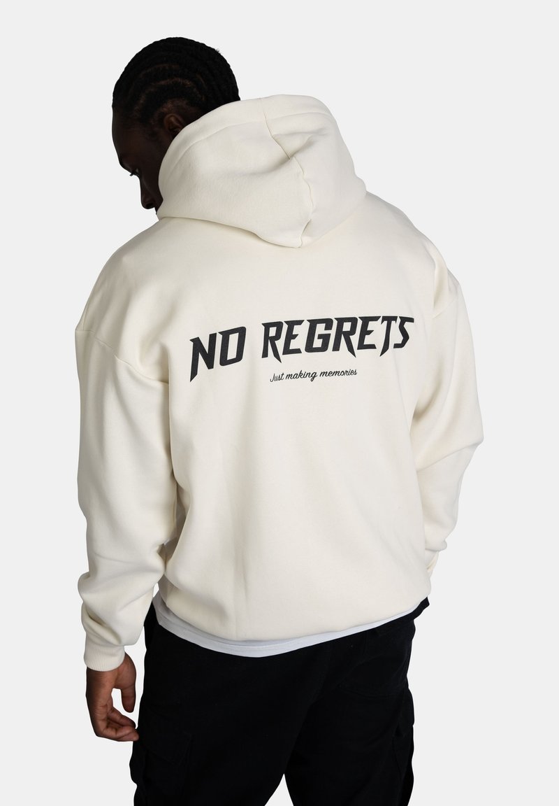 Felpa con cappuccio di colore crema e vestibilità oversized. Sul retro presenta la scritta "NO REGRETS" in carattere grassetto nero con testo più piccolo sottostante. Tessuto morbido.