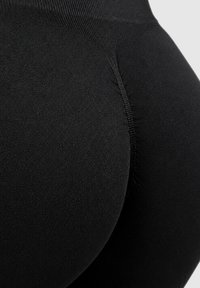 Close-up van een persoon die strakke zwarte naadloze leggings draagt, met zichtbare stoftextuur en stiksel details op het heupgebied.