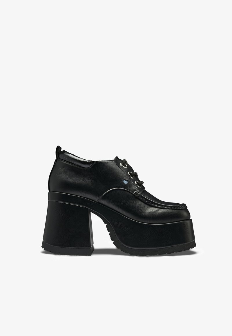 Zwart chunky plateau schoen met dikke hoge hak, vetersluiting aan de voorkant en moc-toe stiksels, zijaanzicht op een witte achtergrond.