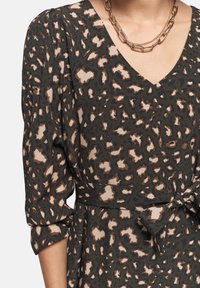 Vestido de estampado de leopardo en verde oscuro, con acentos en beige y marrón. Presenta escote en V, mangas de tres cuartos y un detalle de cinturón en la cintura.