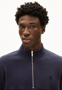 Sweat à fermeture éclair navy en tissu doux avec col haut, arborant un petit logo brodé sur la poitrine et un détail de fermeture éclair argenté.