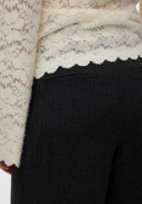 Kanten top in crème met bloemmotief en gezoomde rand, gecombineerd met donkergrijze op maat gemaakte pantalon met achterzakdetails.