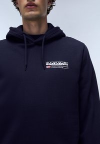 Felpa blu navy con tasca a canguro, cappuccio con cordino e una patch logo testurizzata sul petto con testo e bandiera.