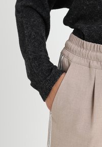 Grå, texturerad långärmad topp i kombination med beige byxor med elastisk midja som har sidofickor och subtila sidosträck.