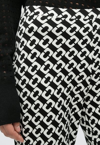 Mustvalged mustriga püksid, millel on geomeetriline disain kattuvate "C"-kujude kujul; kangas tundub sile ja veidi läikiv.