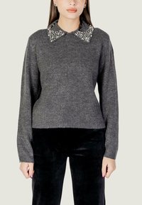Grijze gebreide trui met lange mouwen, voorzien van een decoratieve kraag versierd met witte parels. De trui heeft een geribbelde zoom. Gecombineerd met zwarte broeken.