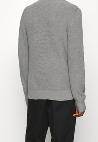 Maglione grigio a maglia con una texture a coste, caratterizzato da un collo rotondo e maniche lunghe. L'orlo e i polsini sono anch'essi a coste, conferendogli una forma strutturata.