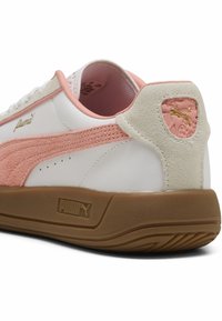 Valkoiset sneakersit, joissa on pehmeät vaaleanpunaiset yksityiskohdat ja nupukkinahkaiset detaljit. Varustettu teksturoidulla kumipohjalla ja kultaisella logolla sivussa ja kantapäässä.