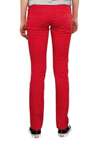 Jeans de algodón rojos con corte ajustado y bolsillos traseros, combinados con zapatillas en blanco y negro. Textura suave y diseño a medida.